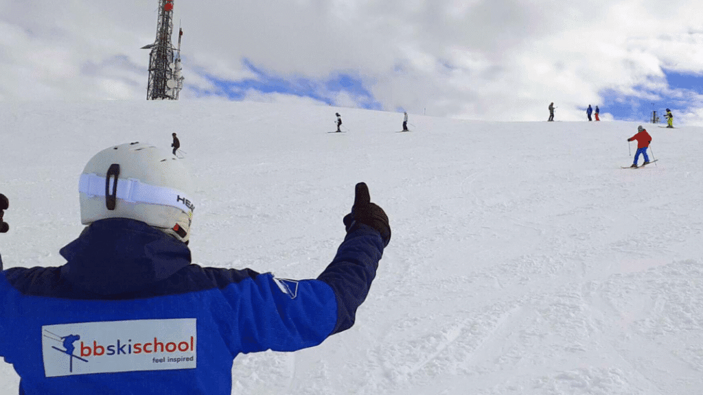 An instructor from Baqueira British Ski School gives the thumbs up while watching skiers descend a wide, snowy slope at Baqueira-Beret ski resort.
