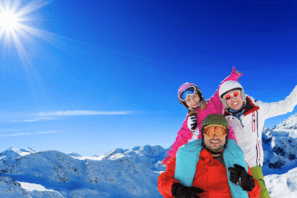 A happy family poses together on a sunny mountain with snowy peaks in the background, illustrating the Best European ski resorts for beginners.
