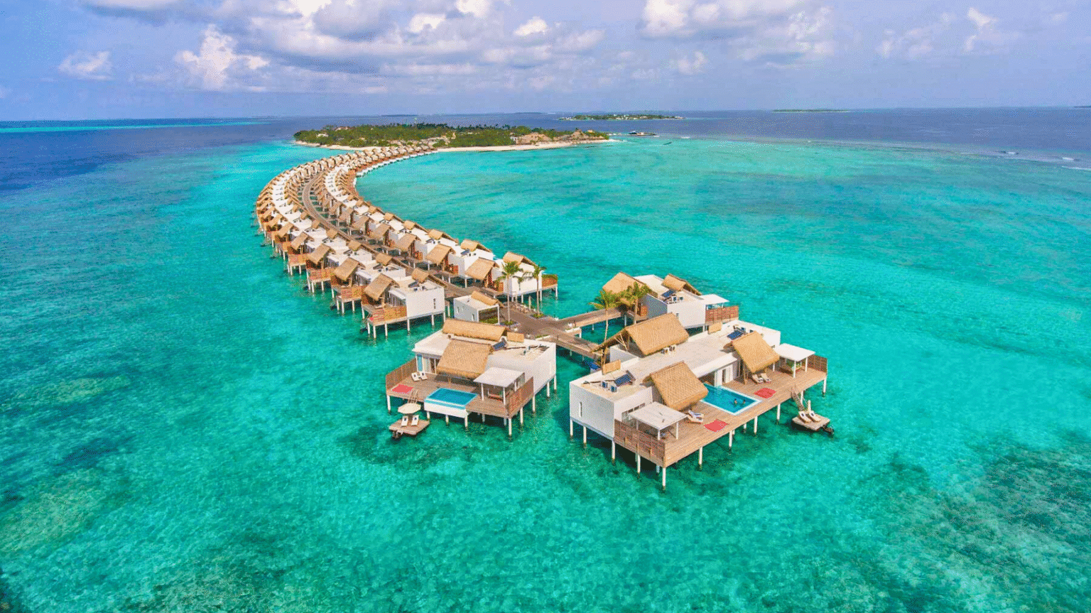 Aerial view of overwater villas stretching in a curve over turquoise waters at the Emerald Maldives Resort & Spa.