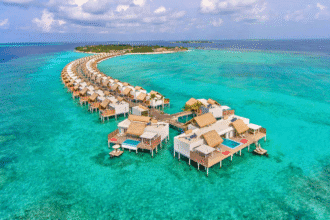 Aerial view of overwater villas stretching in a curve over turquoise waters at the Emerald Maldives Resort & Spa.