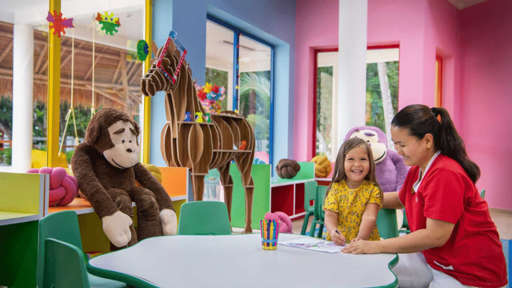 A smiling child and a staff member colour together in the brightly decorated kids’ club at Emerald Maldives Resort and Spa, surrounded by toys and colourful furniture.