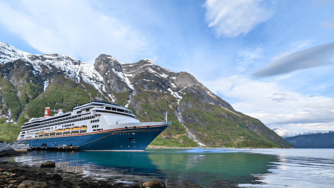 Fred. Olsen cruise ship Bolette docked beside a fjord with snow-capped mountains in Norway.