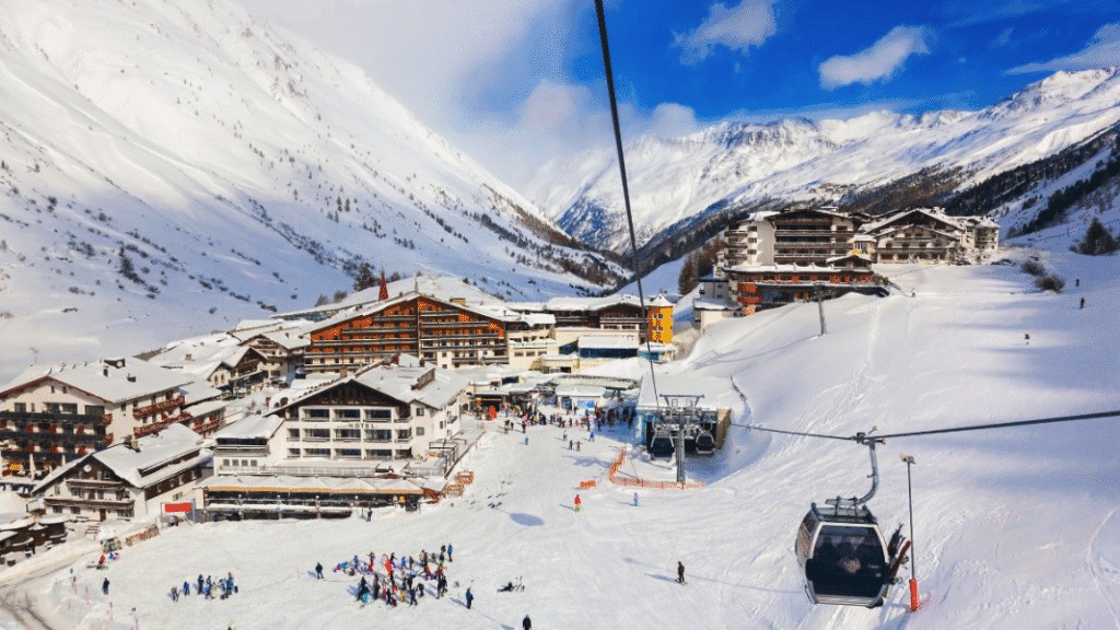 Obergurgl ski resort with hotel buildings clustered beside snowy slopes, ski lifts, and beginners practising on wide, gentle runs.