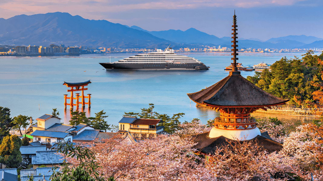 Scenic Eclipse cruise ship anchored off Miyajima Island, Japan, with cherry blossoms, a traditional pagoda, and the iconic floating Torii gate in the scene.