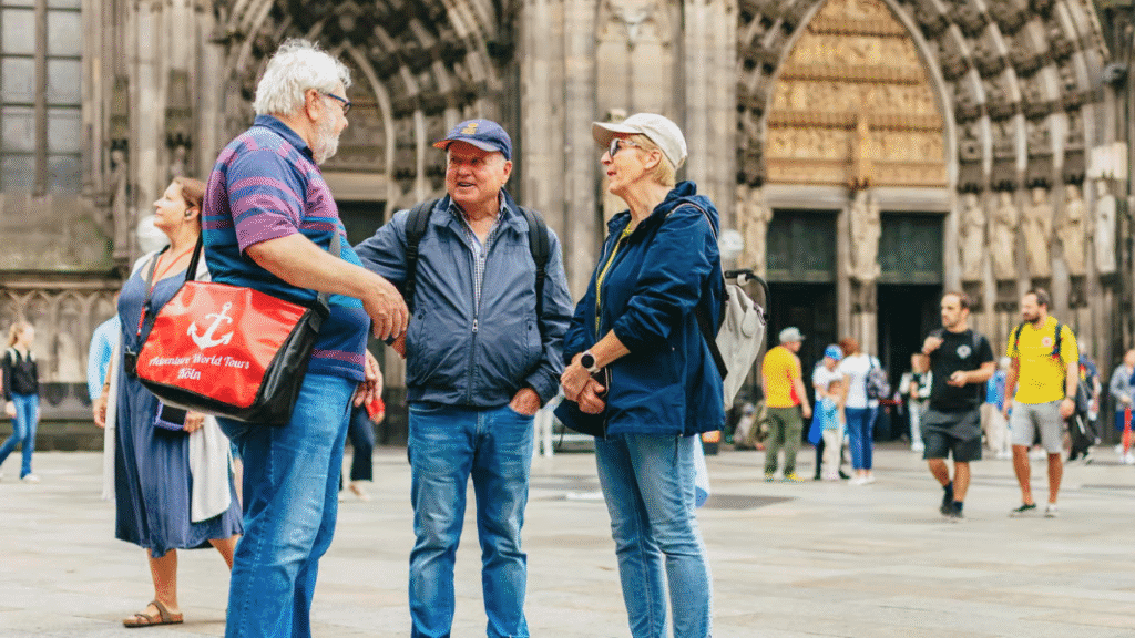 A group of older tourists chat outside a historic cathedral in a European city, taking part in a guided tour as part of a river cruise holiday.